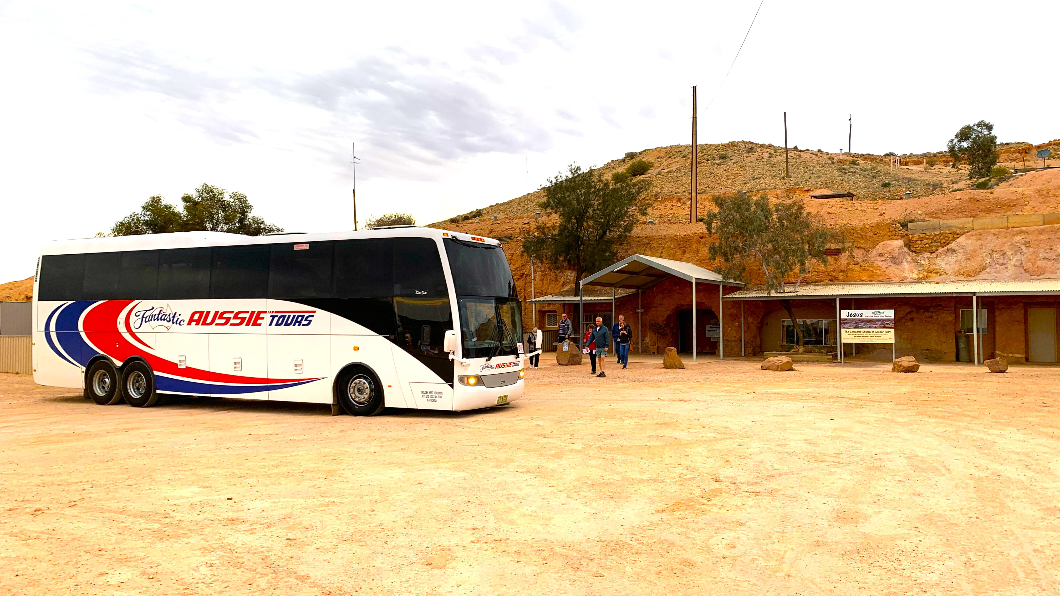 A CFT/Fantastic Aussie Tours liveried bus sits outsite the Catacomb Church in Coober Pedy on a past tour